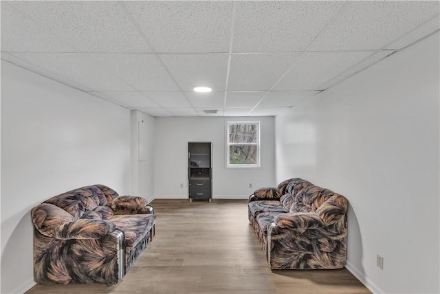 living area featuring a paneled ceiling, visible vents, baseboards, and wood finished floors