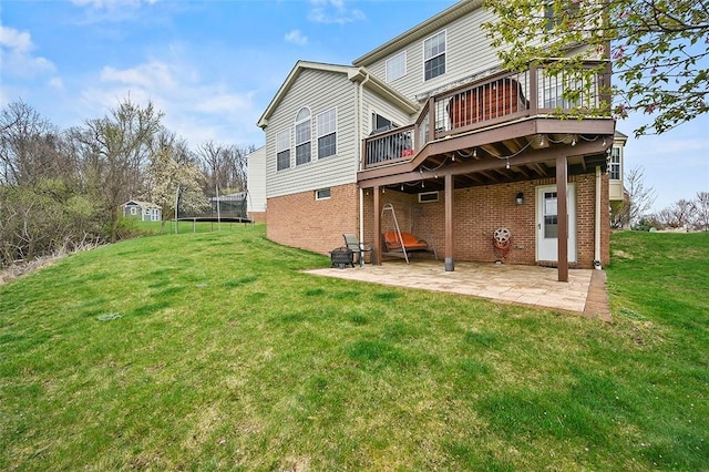 back of house featuring a lawn, a deck, a trampoline, and a patio area
