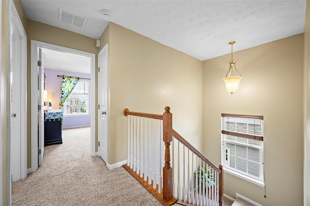 hall with visible vents, baseboards, light carpet, and an upstairs landing