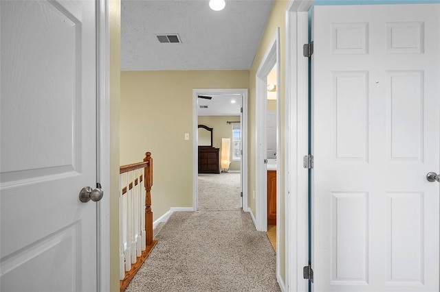 hall featuring baseboards, light colored carpet, visible vents, and an upstairs landing