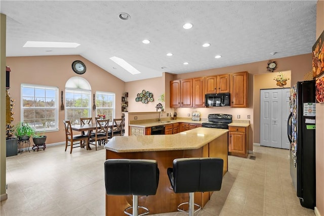 kitchen with a kitchen island, a breakfast bar area, recessed lighting, a sink, and black appliances