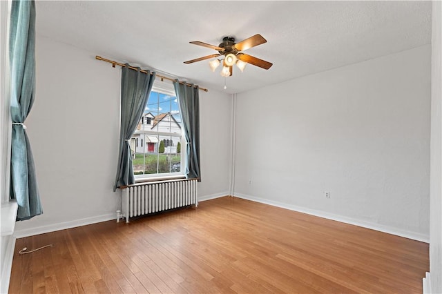 spare room with baseboards, ceiling fan, wood finished floors, and radiator heating unit