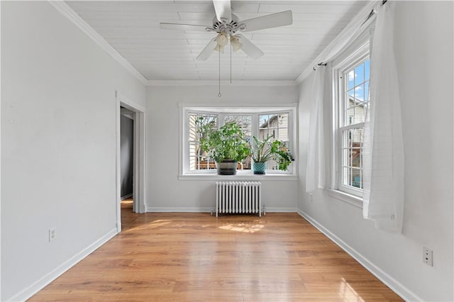 spare room featuring a wealth of natural light, radiator heating unit, crown molding, and light wood finished floors