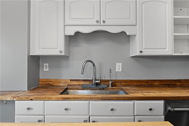 kitchen with wooden counters, white cabinetry, and a sink