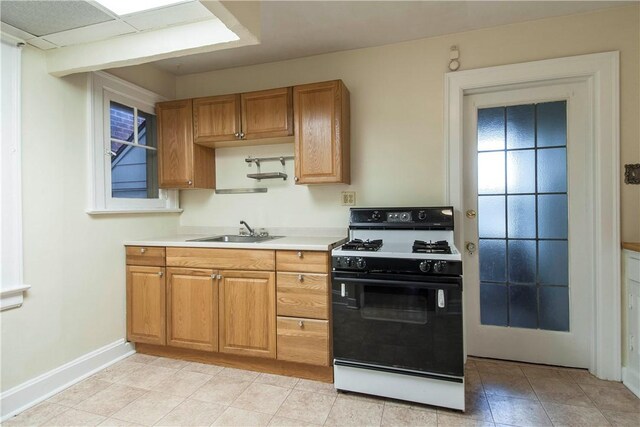 7447 Schoyer Ave, Swissvale, PA 15218 - kitchen featuring light countertops, a sink, brown cabinetry, gas range oven, and baseboards