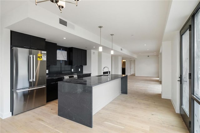 kitchen featuring visible vents, appliances with stainless steel finishes, a sink, dark cabinetry, and light wood finished floors