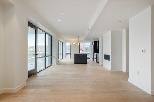 corridor featuring light wood-style floors, a notable chandelier, and baseboards