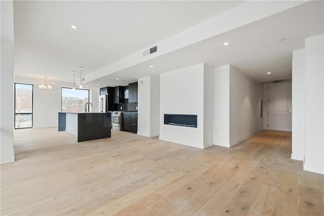 unfurnished living room with a fireplace, visible vents, a sink, light wood finished floors, and a notable chandelier