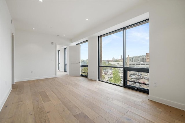 empty room with recessed lighting, a city view, light wood-style flooring, and baseboards