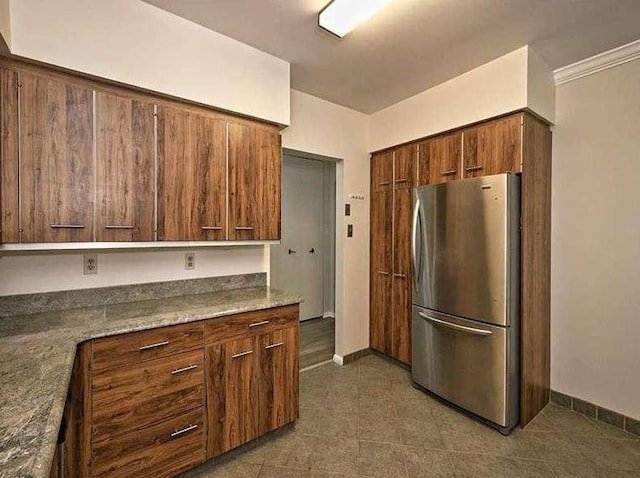 kitchen featuring brown cabinets, freestanding refrigerator, and baseboards