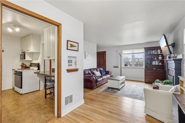 living room with light wood-style floors, visible vents, and baseboards