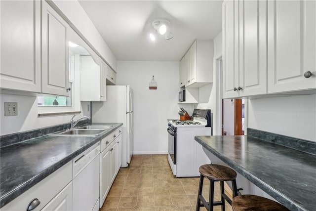 kitchen with a sink, white cabinets, dark countertops, and white appliances