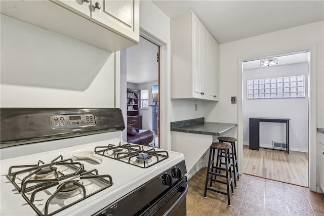 kitchen featuring white range with gas cooktop, visible vents, white cabinets, dark countertops, and baseboards