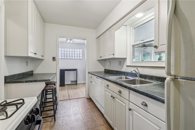 kitchen with a sink, dark countertops, white appliances, and white cabinetry