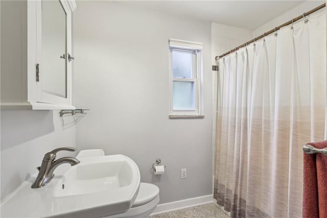 bathroom featuring toilet, curtained shower, a sink, and baseboards
