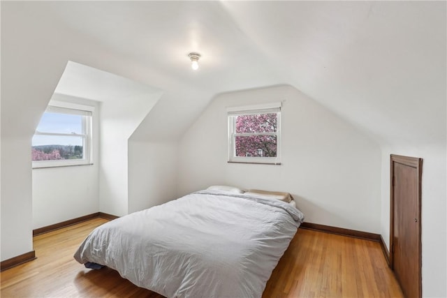 bedroom with light wood-style floors, baseboards, and vaulted ceiling