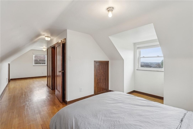 bedroom with light wood-type flooring, multiple windows, vaulted ceiling, and baseboards