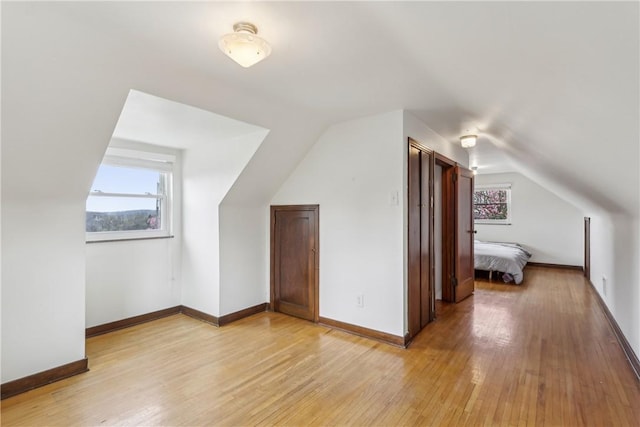 additional living space with light wood-type flooring, baseboards, and vaulted ceiling