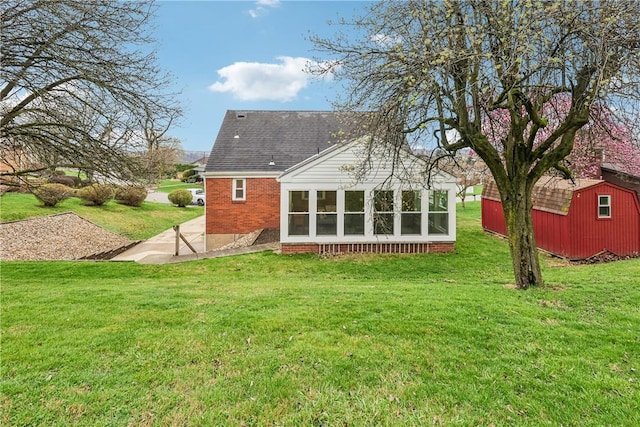 rear view of property featuring an outbuilding, a storage shed, a sunroom, a yard, and brick siding