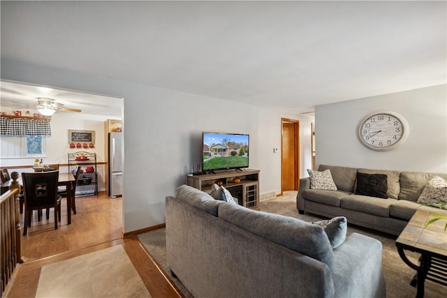 living room featuring light wood-type flooring, baseboards, and ceiling fan