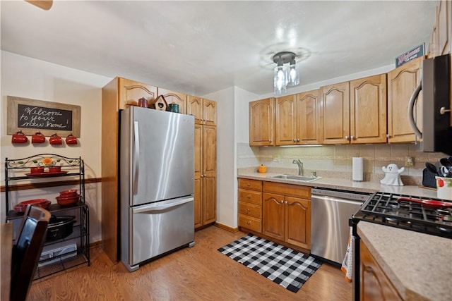 kitchen with light wood-style floors, light countertops, a sink, stainless steel appliances, and decorative backsplash