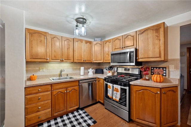 kitchen with appliances with stainless steel finishes, light countertops, decorative backsplash, light wood finished floors, and a sink