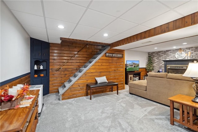 carpeted living room with a fireplace, a wainscoted wall, wood walls, stairs, and a drop ceiling