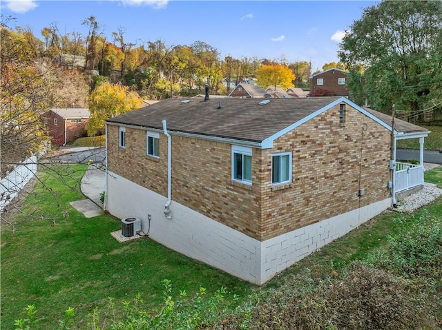 view of side of property featuring roof with shingles, a yard, brick siding, and central air condition unit