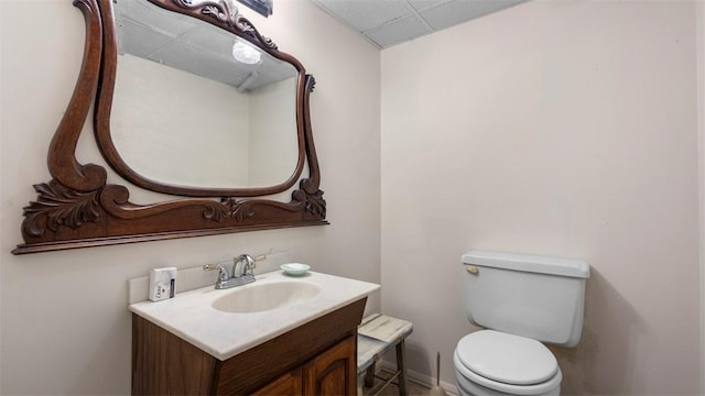 half bath featuring toilet, a paneled ceiling, and vanity