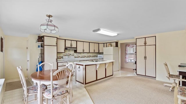 kitchen featuring white appliances, an island with sink, light countertops, under cabinet range hood, and hanging light fixtures
