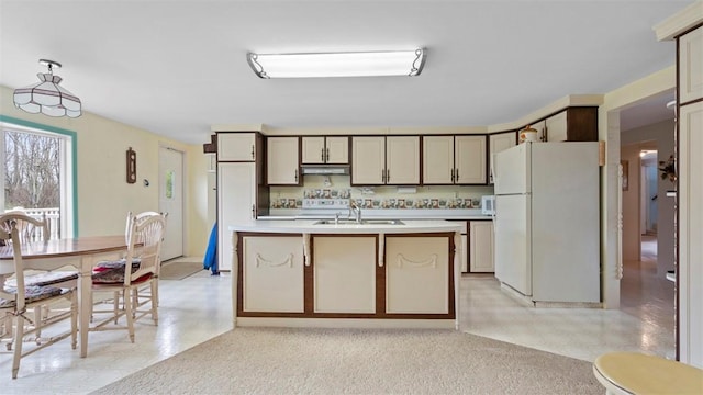 kitchen featuring white appliances, light countertops, under cabinet range hood, a kitchen island with sink, and a sink