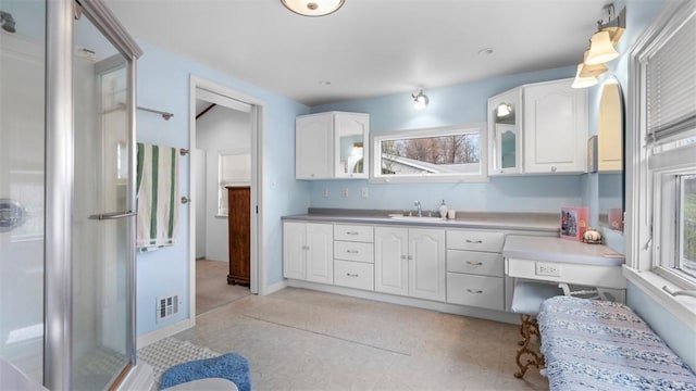 kitchen with white cabinets, glass insert cabinets, visible vents, and a sink