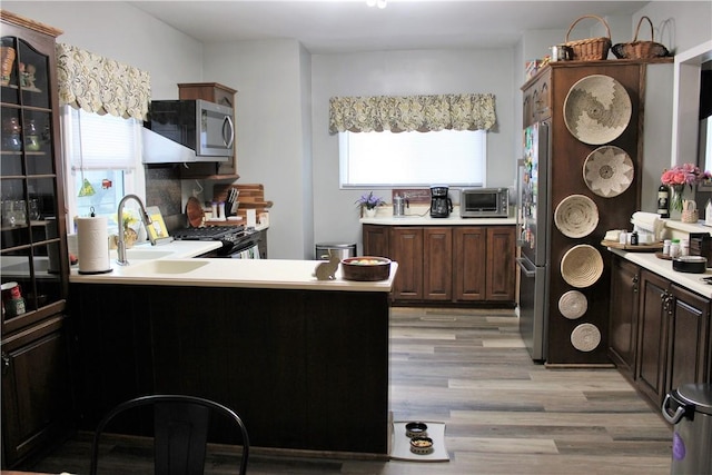 kitchen with appliances with stainless steel finishes, light wood finished floors, light countertops, and dark brown cabinets