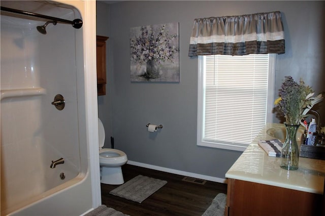 bathroom featuring wood finished floors, baseboards, toilet, vanity, and tub / shower combination
