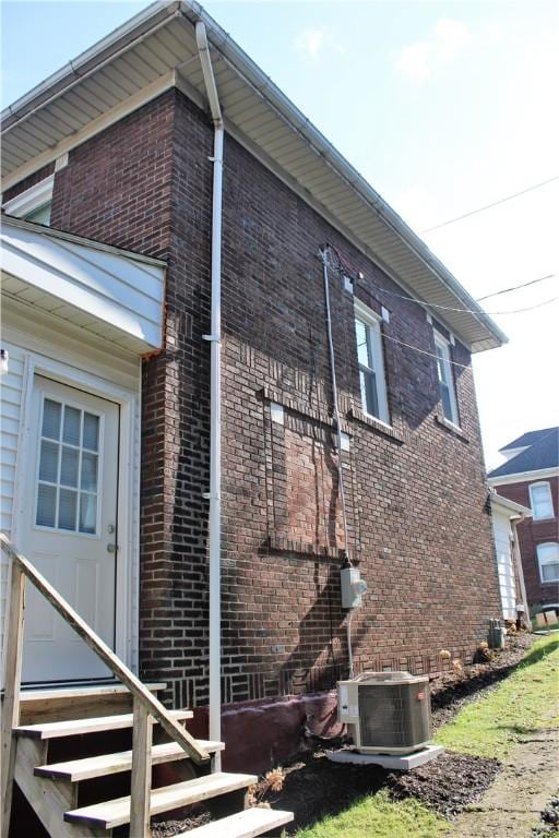 view of property exterior featuring brick siding, entry steps, and central AC