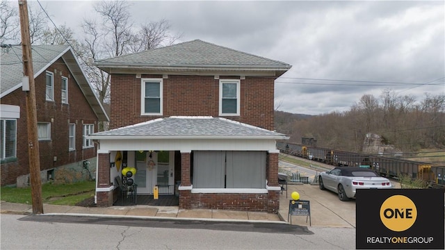american foursquare style home with roof with shingles, brick siding, a porch, and fence