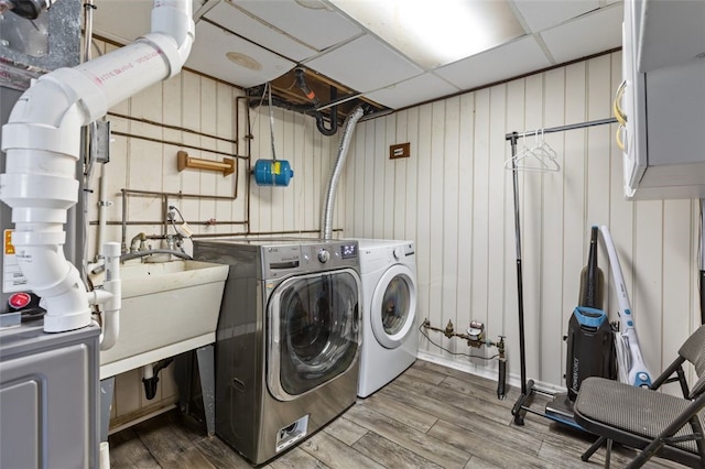 clothes washing area with a sink, independent washer and dryer, and wood finished floors