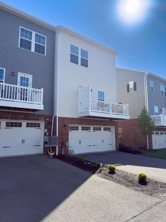 rear view of house featuring driveway, an attached garage, brick siding, and a balcony