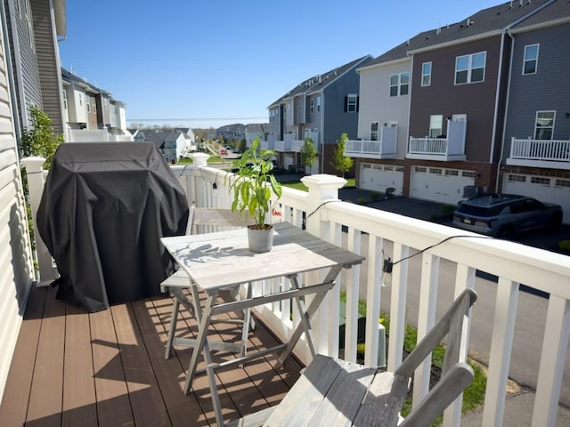 deck with an attached garage, outdoor dining area, a residential view, and a grill