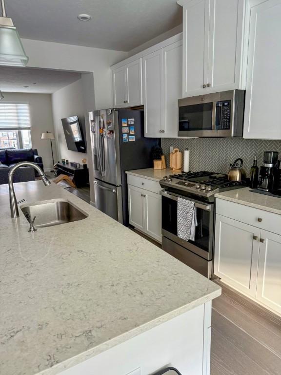 kitchen featuring white cabinetry, a sink, stainless steel appliances, light wood finished floors, and backsplash