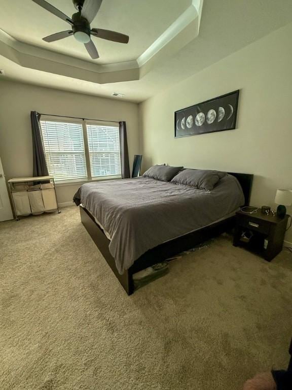 carpeted bedroom featuring ceiling fan, crown molding, and a tray ceiling