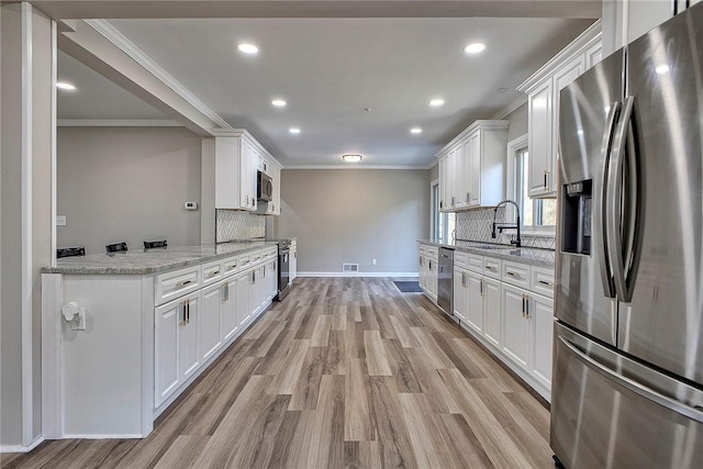 kitchen with white cabinetry, ornamental molding, a sink, stainless steel appliances, and backsplash
