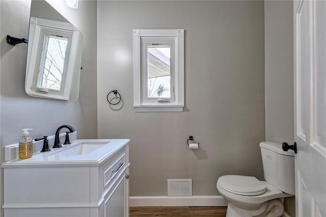 half bathroom featuring toilet, vanity, visible vents, and plenty of natural light