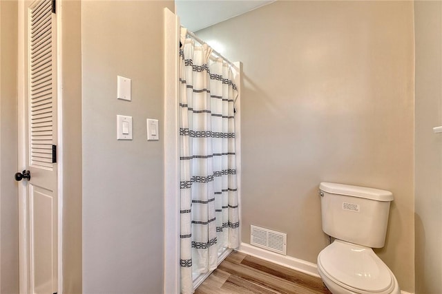 bathroom featuring a shower with shower curtain, baseboards, toilet, visible vents, and wood finished floors