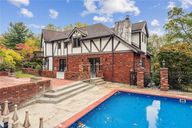 back of property featuring stucco siding, fence, brick siding, an outdoor pool, and a chimney