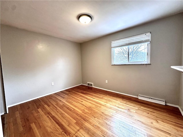 empty room featuring visible vents, baseboards, hardwood / wood-style floors, and a baseboard heating unit