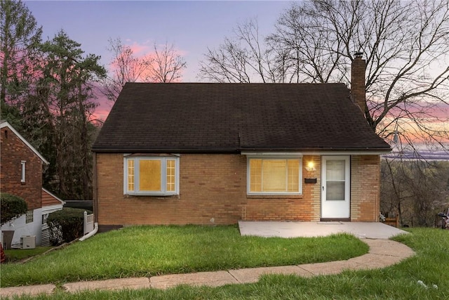 view of front of house featuring a patio area, a front lawn, brick siding, a chimney, and a shingled roof