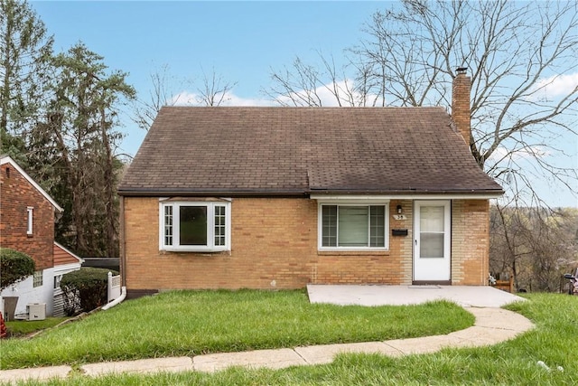 cape cod-style house with a shingled roof, a patio area, a chimney, brick siding, and a front lawn