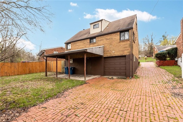 back of property with brick siding, an attached garage, fence, and decorative driveway