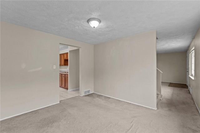 unfurnished room with baseboards, visible vents, light colored carpet, and a textured ceiling
